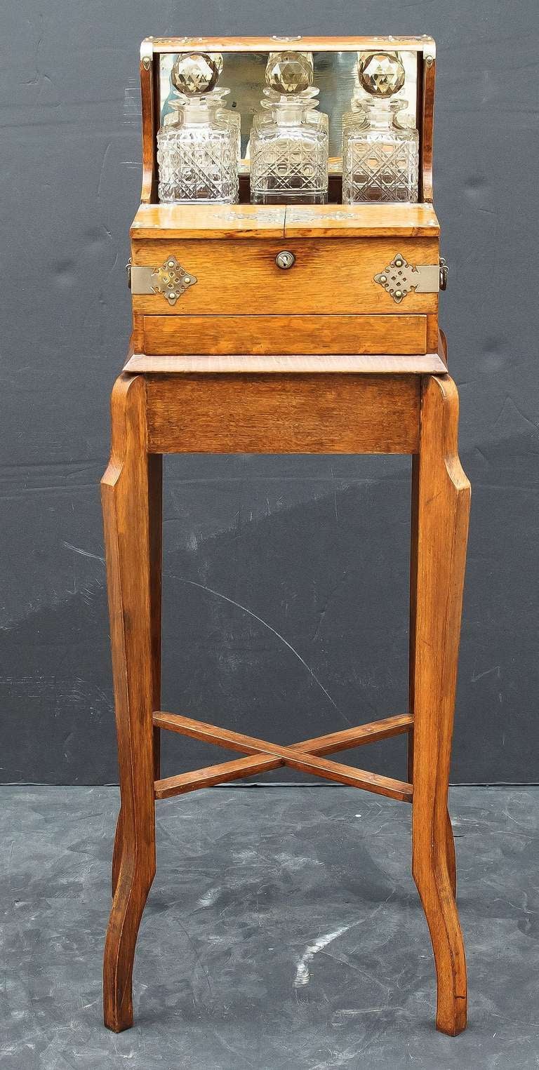 An English tantalus and games box set, in a brass-bound, fitted oak case having a hinged lid with mirrored back.
The interior fitted with three cut-glass decanters with faceted, spherical stoppers, behind a locking cigar or tobacco compartment,