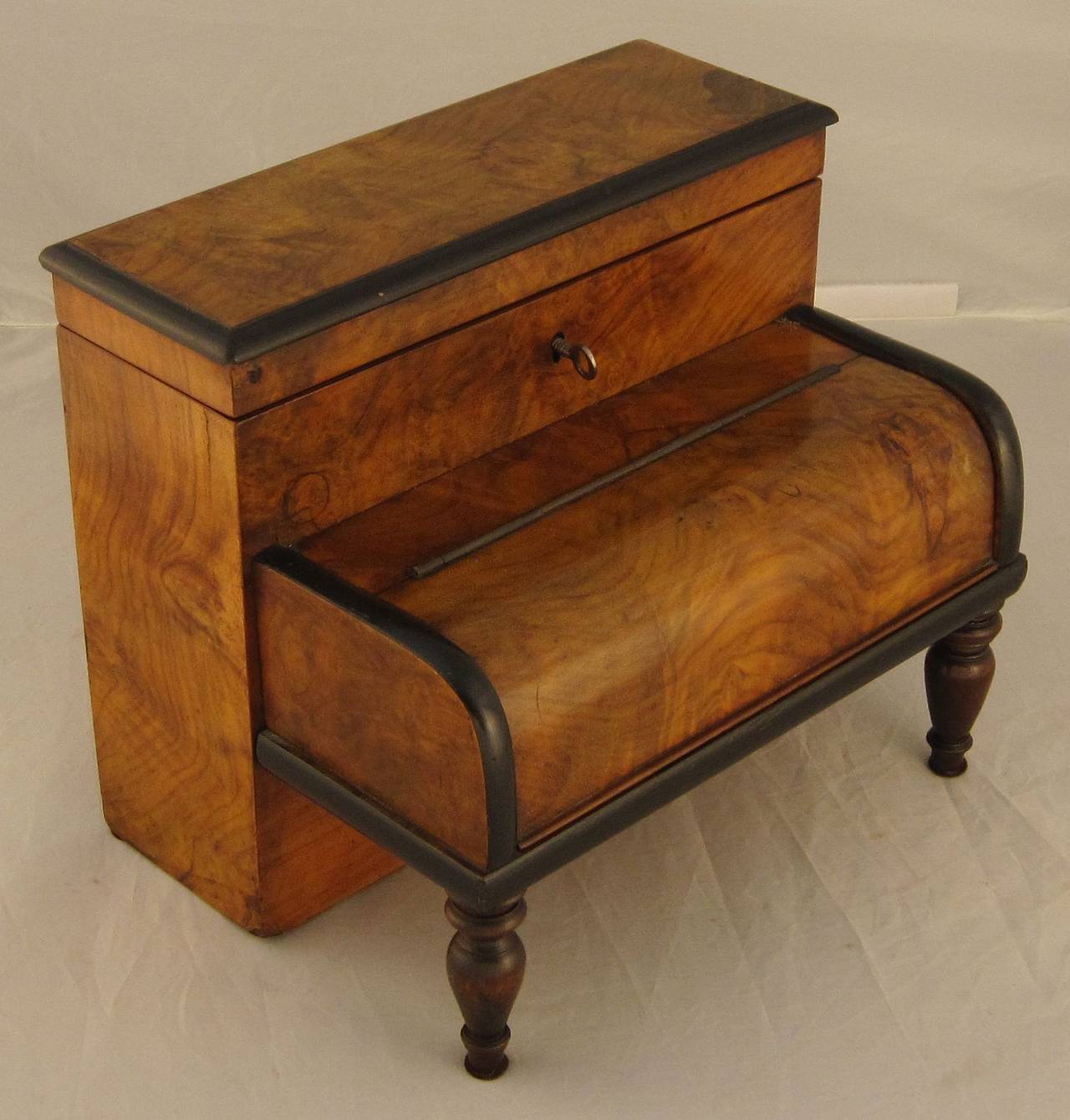 A fine English desk set and stationery box of burled walnut with ebonized accents, in the novelty form of a stand-up piano.
Featuring a stationery box with hinged lid mounted to a moulded compartment with hinged cover, on two turned legs, opening