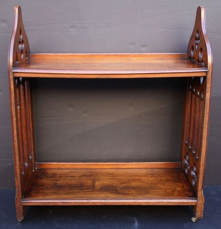 A fine English standing bookcase of oak in the Gothic style favoured by the famous British family of architects, the Pugins. Featuring two handsomely-patinaed tiers, each with gallery back, joined by two arched panels with carved quatrefoils, set