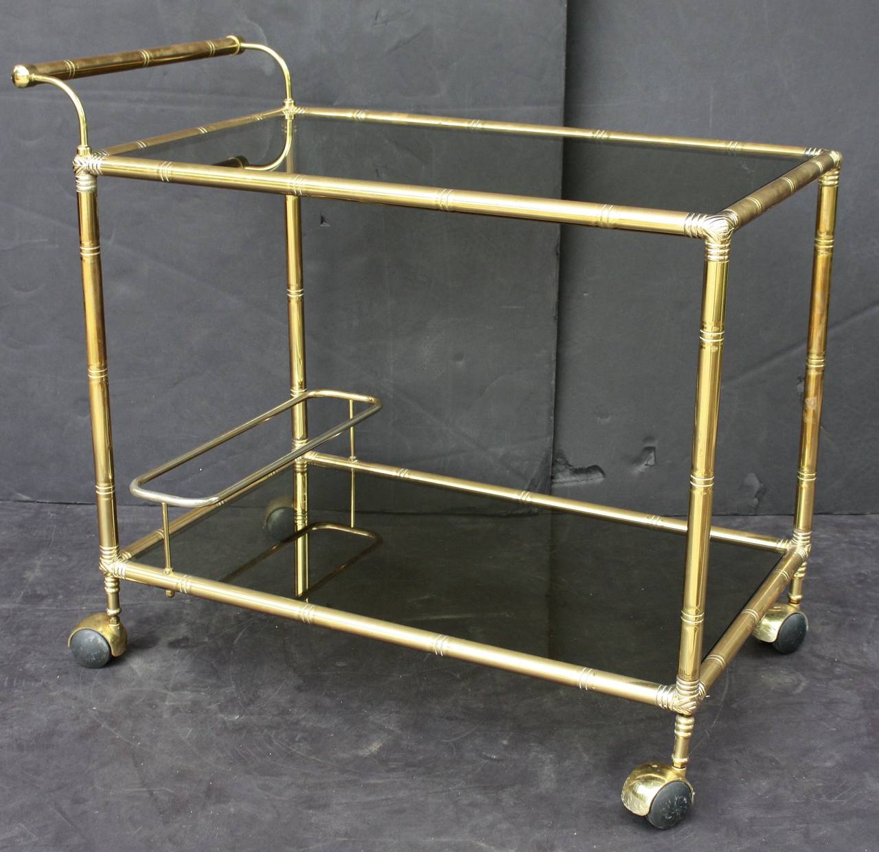 A vintage French rectangular bar cart table or serving trolley in brass with a bamboo design, and featuring two smoked glass tiers, on rolling caster wheels. 

Perfect for use as a side or end table.