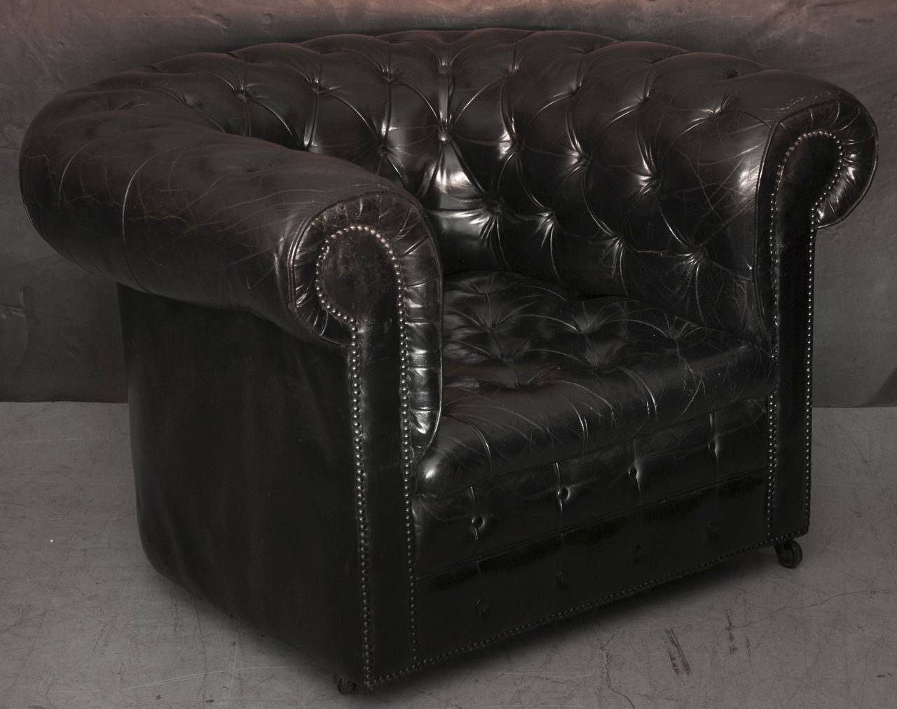 A handsome pair of English Chesterfield club chairs in black or ebony leather. Each chair featuring tufted leather back and seat, rolled arms with brass nail heads trim and rolling casters. With deep seats for comfort and in excellent condition.