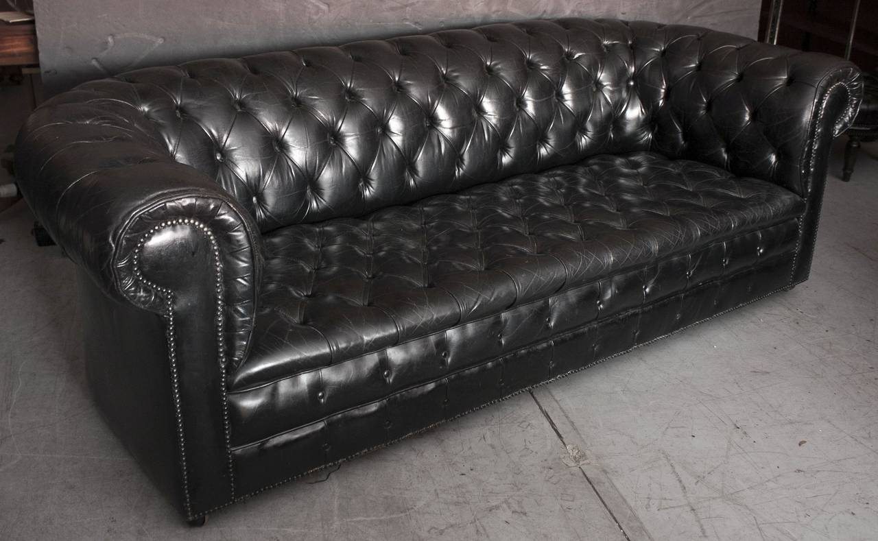 A fine English large Chesterfield sofa in vintage black or ebony leather featuring button-tufted back and arms with beaded-nail trim design, resting on rolling caster wheels.

The Chesterfield Sofa is a classic, synonymous with English design.