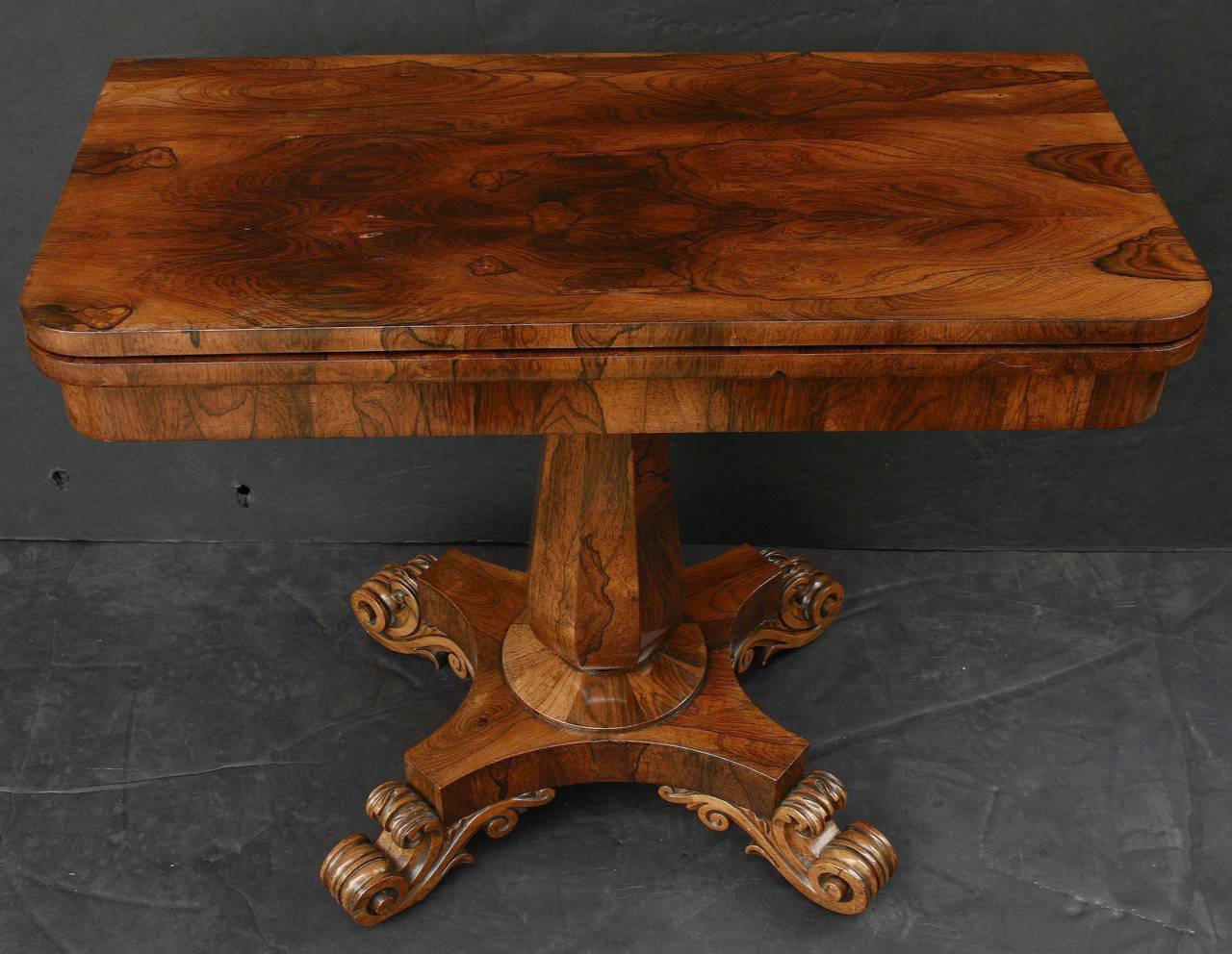 A handsome English game or card table (or tea table) of rosewood, featuring a fold-over, sliding top of figured rosewood, rotating and opening to a square felt-covered top for entertaining. Set upon a faceted column post and four-legged base with