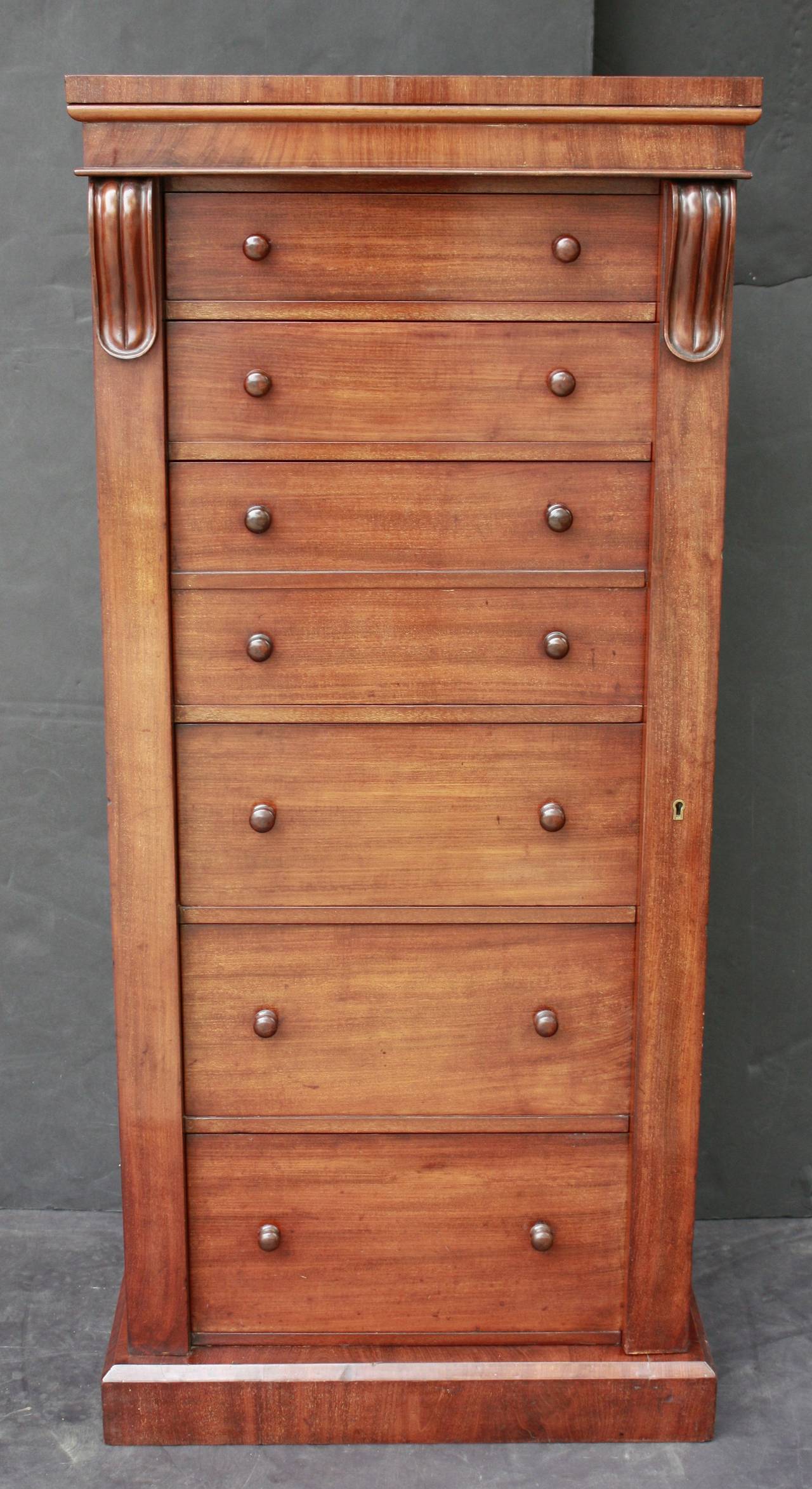 An English cabinet or chest of mahogany, fondly known as a Wellington, featuring a moulded top over six drawers of ascending size (top to bottom). 
The third and fourth drawers with faux front (giving an overall appearance of seven drawers),