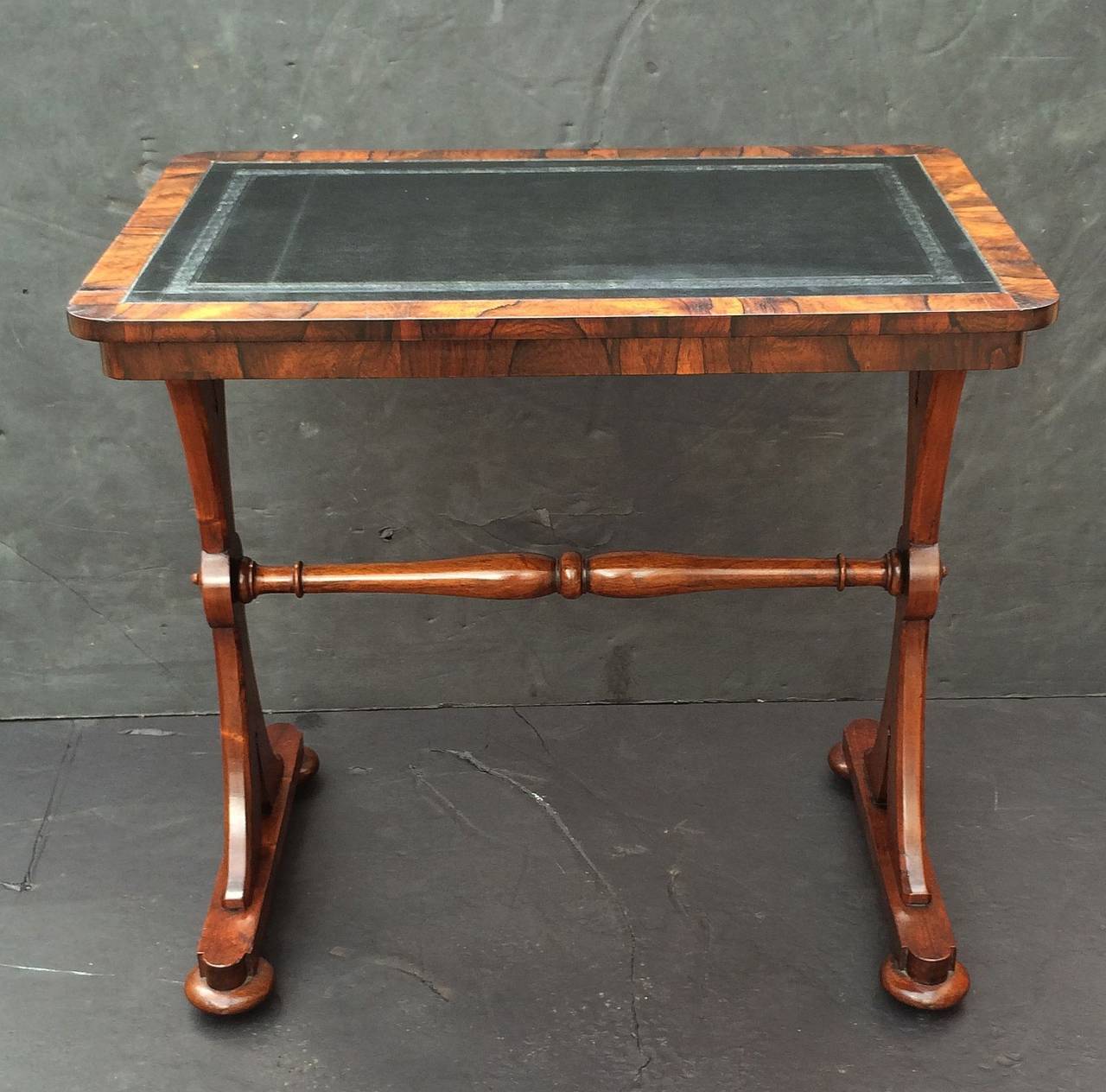 A handsome English writing or side table, featuring a moulded rosewood top with inset surface of embossed black leather, mounted to a frieze with turned support stand of rosewood.