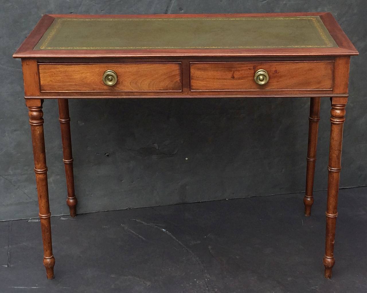 A fine English writing table or desk, featuring a moulded mahogany and gilt embossed green leather inset top over a frieze of two beaded drawers, each with brass hardware, and set upon four turned legs.