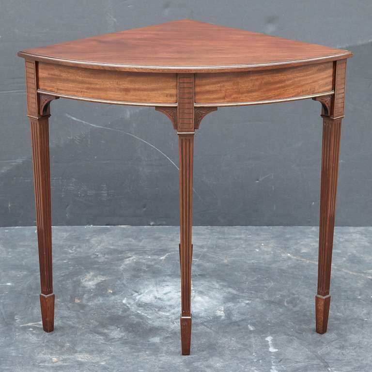 An English corner table of mahogany set upon four tapered legs, featuring a moulded top set upon a frieze with bowed front and decorative spandrels between the legs.

Might make a great side or end table or bedside stand.