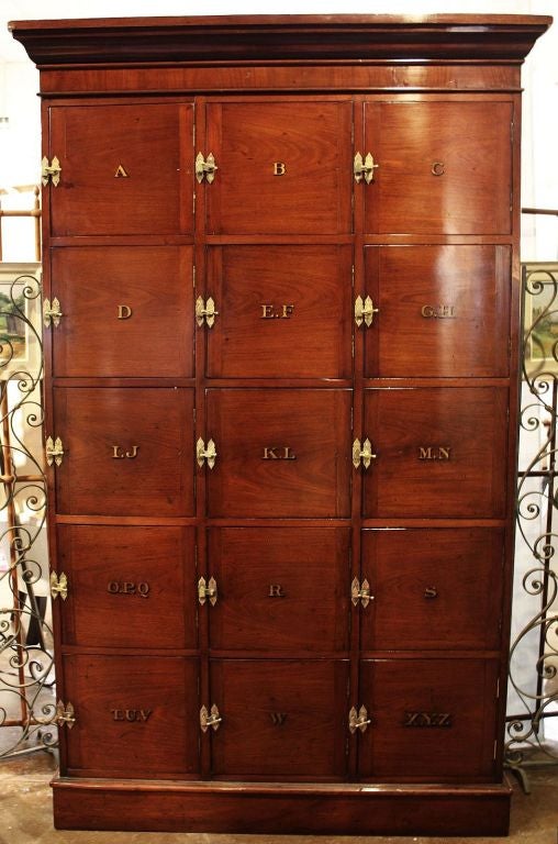 An English barrister's locker of Cuban mahogany with handsome brass hardware and lever locks. <br />
Used in a solicitor's office (law firm), most likely for storage of client files, the locker features a crown moulding over fifteen cubicle