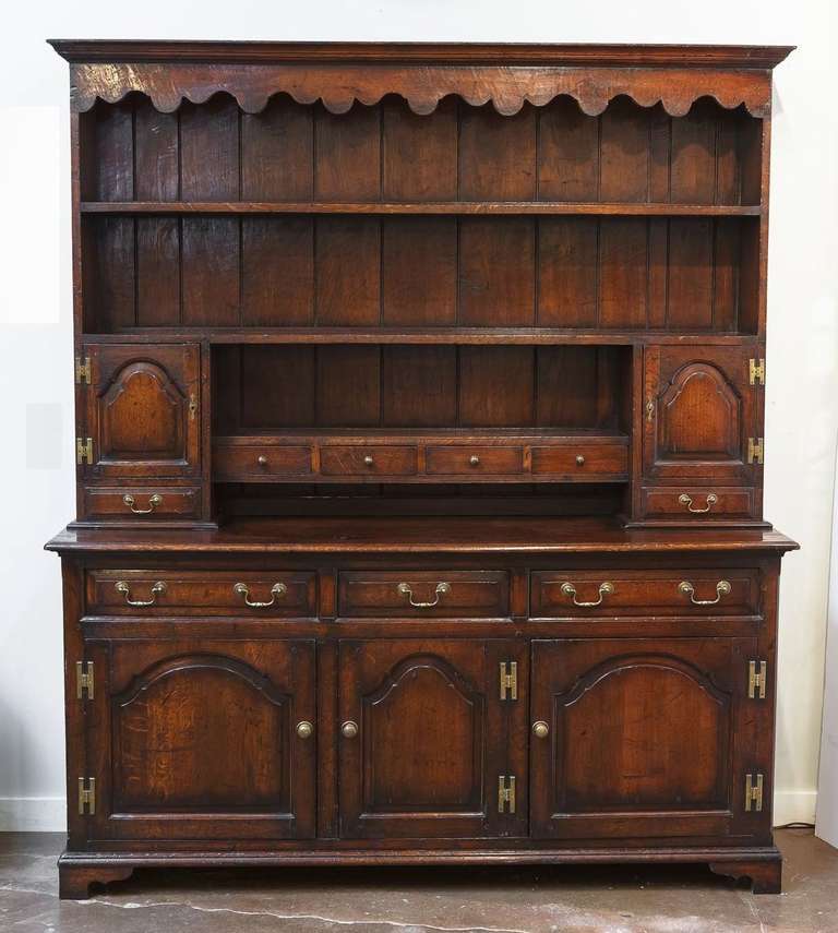 A handsome Welsh cupboard dresser of oak featuring a moulded canopy top with decorative ogee over a three-shelf upper tier with paneled back, flanking cupboards and spice rack, mounted to a dresser base with three drawers over three moulded cupboard