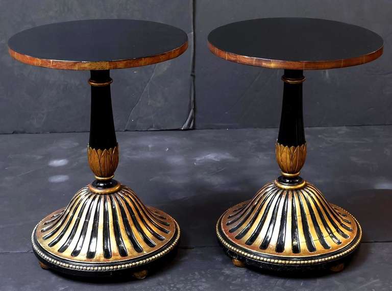 A handsome pair of ebonised, lacquered, and gilt round or circular tables in the Regency or Empire style, with laurel leaves around the column supports and a ribbed design around the circumference of the bases, resting on gilt ball feet.

Would