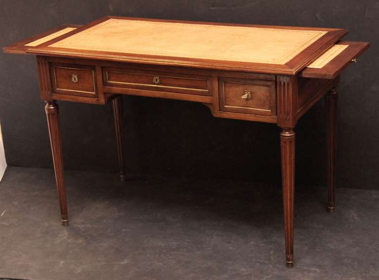 A handsome French writing desk or table of mahogany featuring a moulded top with embossed leather top, over a frieze with three beaded drawers, the opposing side with faux drawer fronts. The brass escutcheons with bee design and two keys. With