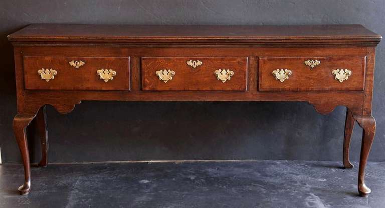 A handsome Welsh dresser base or console server sideboard from the Georgian-era featuring a handsome, patinated oak top and sides with three drawers, each with inlaid cross-banding accents of mahogany, showing pulls and escutcheons of a lovely