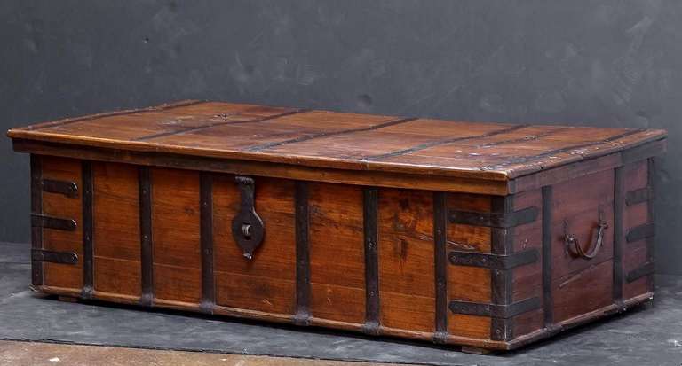 A large rectangular English trunk or coffer chest of iron-bound teak from the Campaign era, featuring a hinged top with iron clasp lock and cross-banded iron base.

Makes a great large low table or cocktail table.
