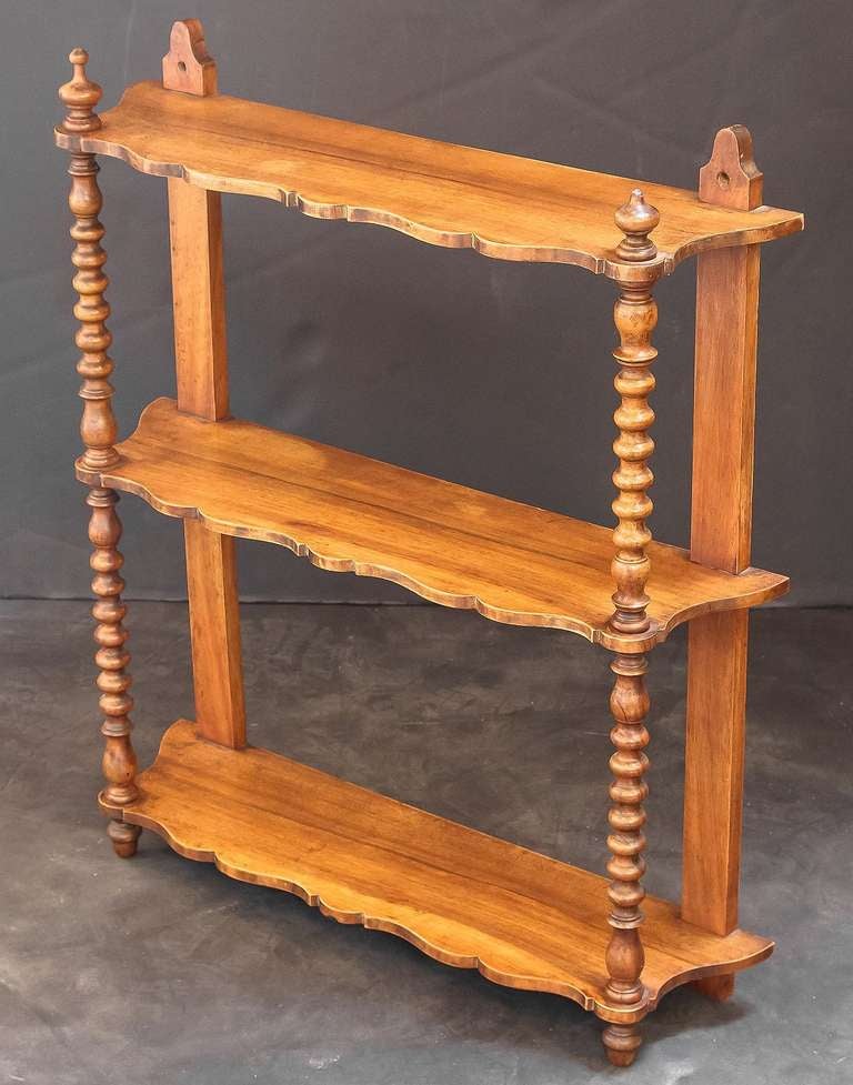 A lovely French hanging curio shelf of walnut featuring three serpentine shelves adjoined by turned wood supports, with decorative finials above the top shelf.