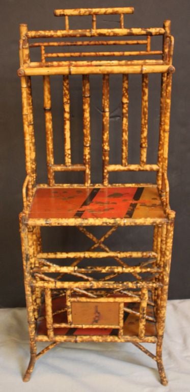 An English Bamboo étagère featuring japan-lacquered shelves on the top, middle, and bottom tiers, fashioned as a canterbury (traditionally, a stand for sheet music) and perfect for use as a magazine rack and stand.<br />
<br />
A nice addition to