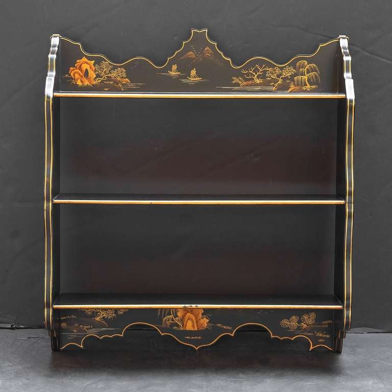 A handsome ebonised or black lacquered hanging wall shelf featuring a chinoiserie design on the top and bottom panels, with gold accents on the shelves and the japanned exterior.