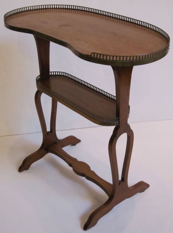 A fine French tiered serving or side table (or tray) or etagere of mahogany, featuring a kidney-shaped upper tier with a pierced brass gallery around three quarters of the circumference, set upon a support of shaped, bowed legs joined with an