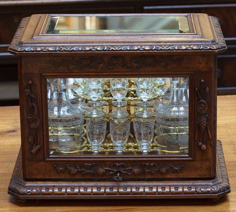 A handsome French tantalus drinks set or Cave a Liqueur
featuring a cabinet of carved walnut and beveled glass with a fitted base, housing a removable Bronze Dore and walnut stand, holding sixteen etched cordial or liqueur glasses, and four etched