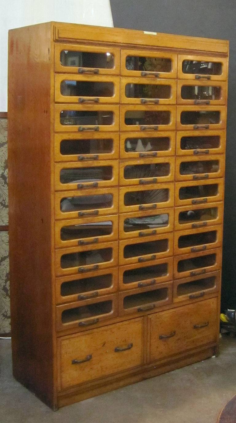 An exceptional haberdasher's or haberdashery cabinet from England featuring:

30 glass-fronted drawers over two blind drawers - 32 drawers total.

Glass-front drawer inside dimensions:
Each drawer H 4 3/4