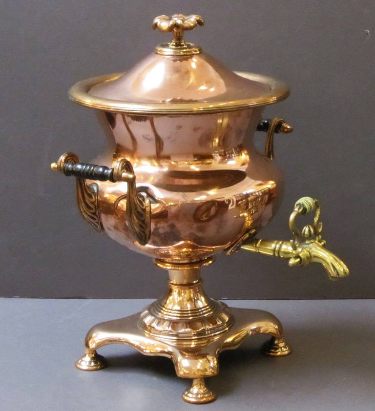 A large French samovar (or tea urn) of copper and brass, featuring a removable domed top with finial, a lovely copper and brass body with ebonized wood handles, a large brass spigot with bone tap, mounted to a footed base.

This item can be used