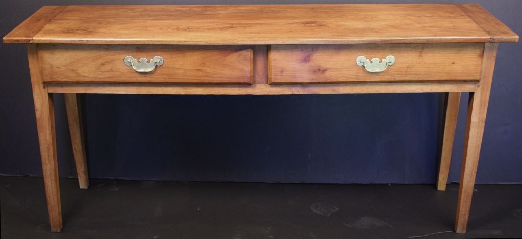 A handsome French console table or buffet server of cherry wood featuring a rectangular plank top over a frieze with two drawers, each with brass pulls, and standing on tapered legs.