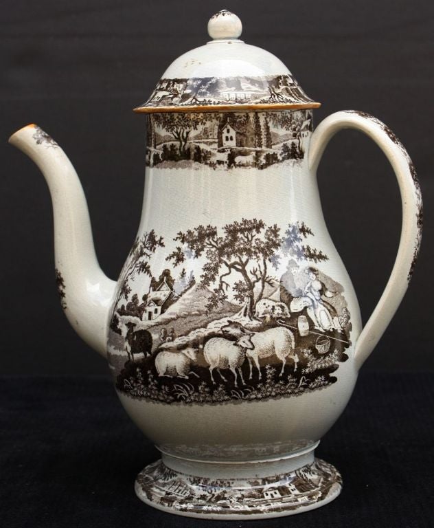 An English coffee pot with lid and serpentine spout featuring a brown and white transferware design of sheep tended by a man and woman, in a pastoral setting.