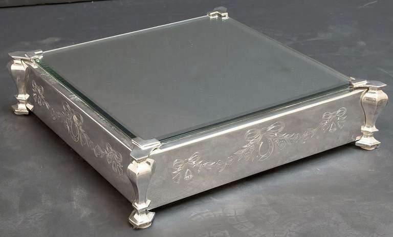 A large English square plateau or centerpiece featuring a beveled, mirrored top mounted to a raised, footed plateau base of plate silver. 
The base with etched decorative design on all four sides showing bells, garlands, and bows.

Perfect for a