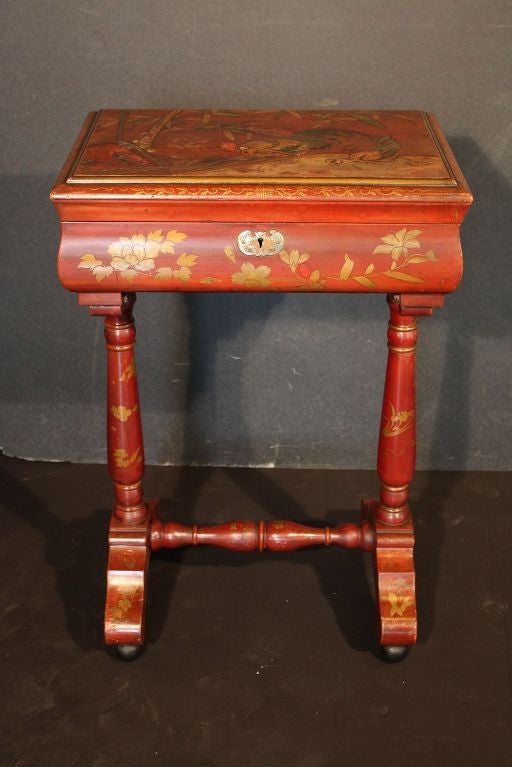 A small chinoiserie box on stand featuring a red Japan-lacquered exterior and a black Japan-lacquered interior.
The top showing a scene of a rooster among stalks of bamboo, foliate designs on the sides and supports, brass escutcheon of a bat, and