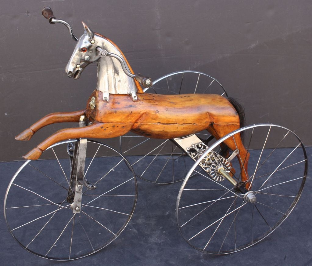 A 19th c. French velocipede or child’s toy tricycle featuring a body of carved wood with brushed steel faceplate and glass eyes, resting on spoke wheels with brass accoutrements and horse-hair tail.

A handsome objet d'art similar to the one