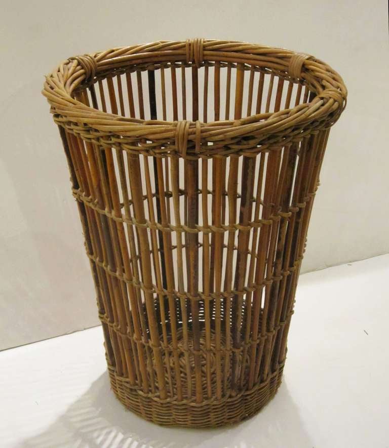A tall English willow basket featuring a cylindrical shape with woven base and top attached to a circular of frame of willow shafts.
