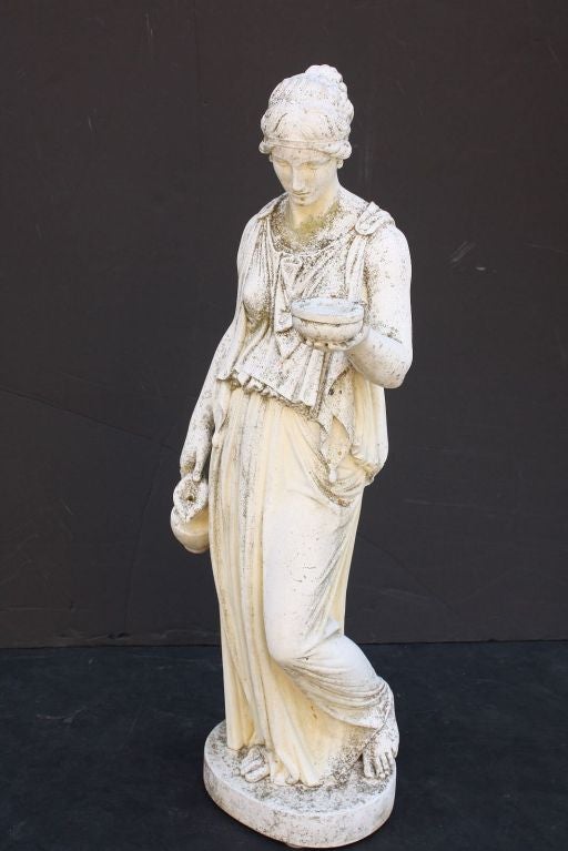 An English garden maiden figure or ornamental statue of composition stone featuring a woman modeled in the Classical style (possibly Hebe who was the cupbearer for the gods and goddesses of Mount Olympus), represented as a robed, standing maiden