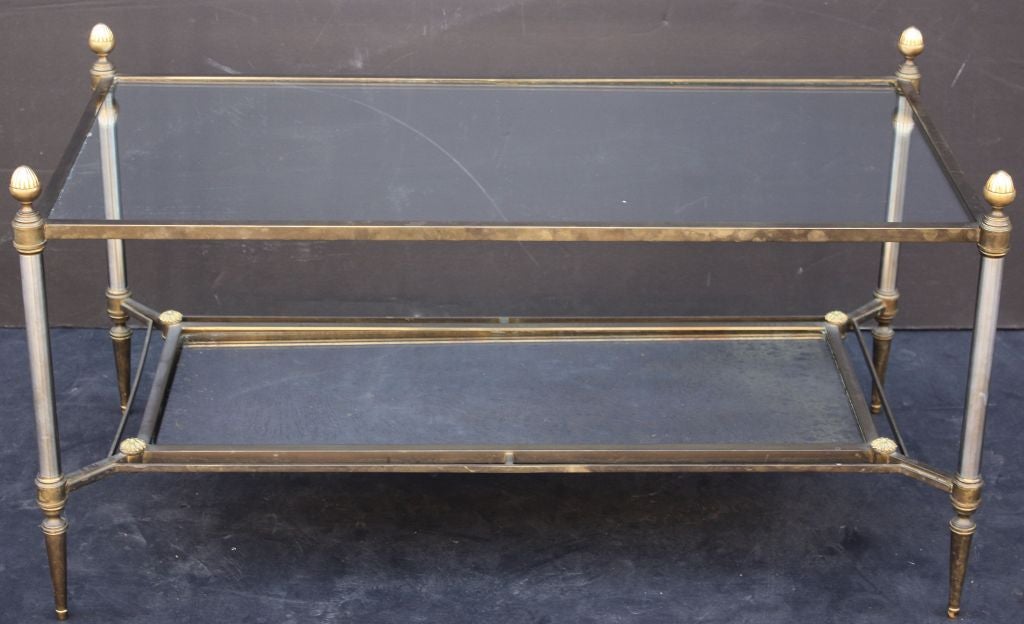A classic French two-tier cocktail or coffee table of gilt bronze and steel, with decorative acorn and floret finials.
Featuring a rectangular clear glass top tier and a patterned smoked mirror bottom tier.