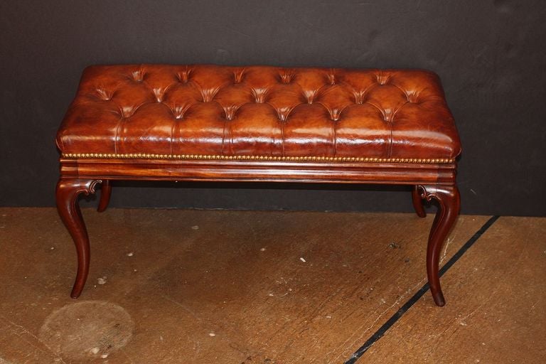 An English Chesterfield bench or sitting stool featuring a button-tufted leather top with nail-head trim over a turned mahogany frieze with handsome cabriole legs.

A pair is available.
Individually priced: $3950 each bench