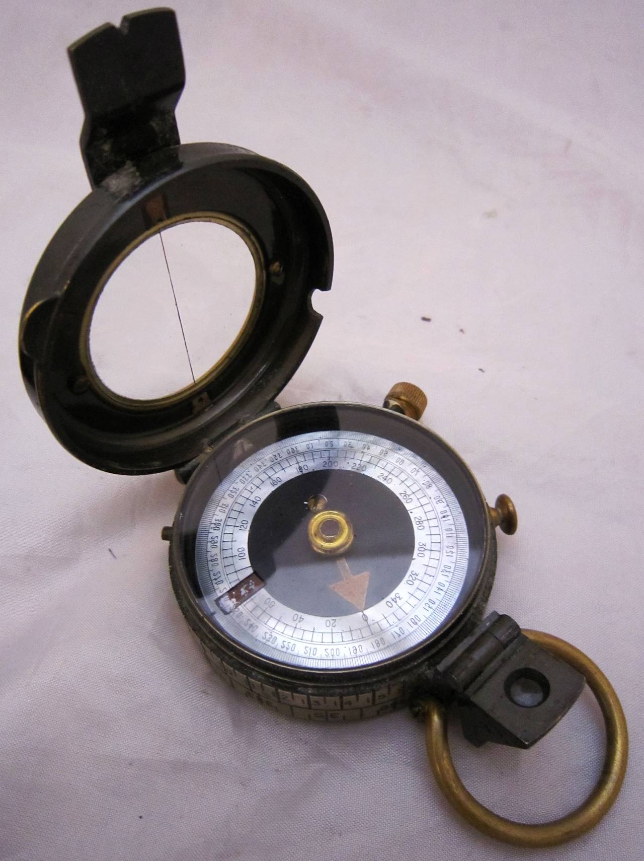 A working British military marching compass of heavy brass in original leather case from World War I. 
Known as a Verner's Pattern VIII prismatic compass, with radium dial.

Back with arrow mark denoting use by the War Office.

Leather case