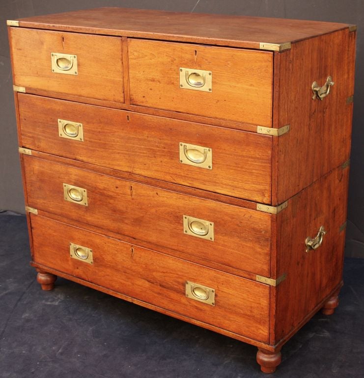 An English military officer’s Campaign Ware chest, featuring a teak exterior, showing two short drawers over three long drawers. The brass-bound chest, in two parts, accented with brass hardware and porter’s handles, resting on shaped