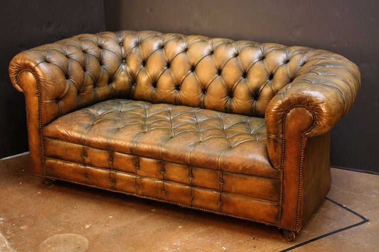 A handsome English Chesterfield sofa (or couch) of leather featuring button-tufted back and arms, soft leather tufted-seat cushion, and beaded-nail trim design, resting on rolling casters.

A classic of English design.