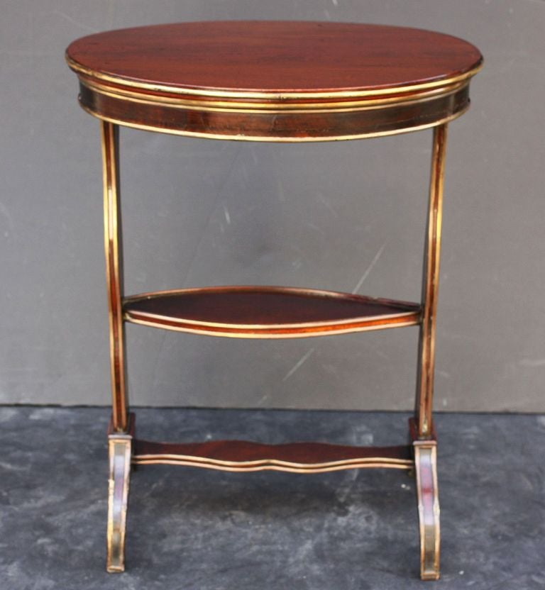A handsome French tiered side or tray table of mimosa wood with bronze trim, known as a vide poche (literally: empty pocket) because of the storage space in the gallery top (with removable lid). The ovoid top fitted to a similarly-shaped middle tier