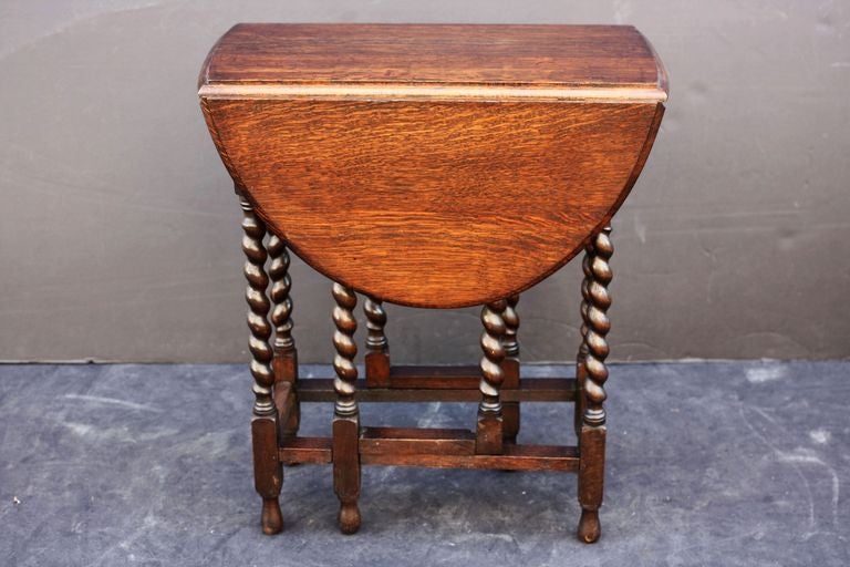 A classic English drop-leaf gateleg table of oak, featuring a moulded top with drop-down sides, over a stretcher of six barley-twist supports.