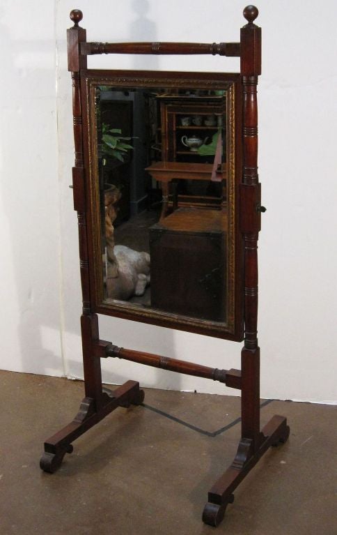 An English cheval mirror from the Regency era featuring turned mahogany frame with finial decoration, framed mirror with gilt accents.