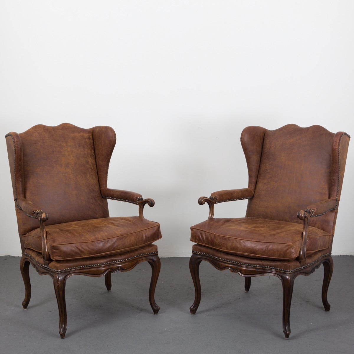 A pair of handsome wingback chairs in oak made in Sweden during the 20th Century in the Rococo style. Upholstered in brown vintage leather, decorated with nail heads.
