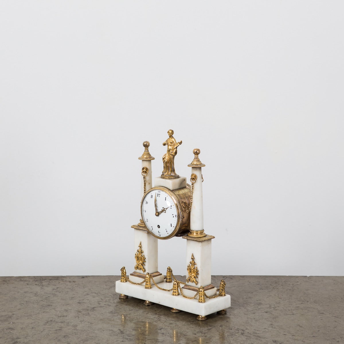 A delicate mantle clock made during the 18th Century in France. White marble with gilt bronze decorations. Working machinery and original enamel face with black arabic numbers. 