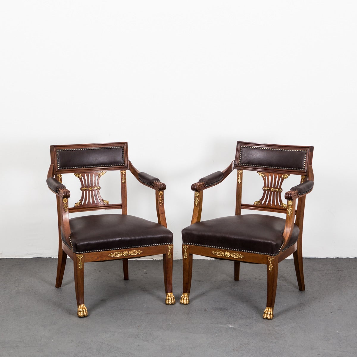 A pair of French desk chairs (can be sold separately as well) made in Mahogany and decorated with polished bronze details. Legs ending with lions feet. 
Upholstered in dark brown vintage leather.