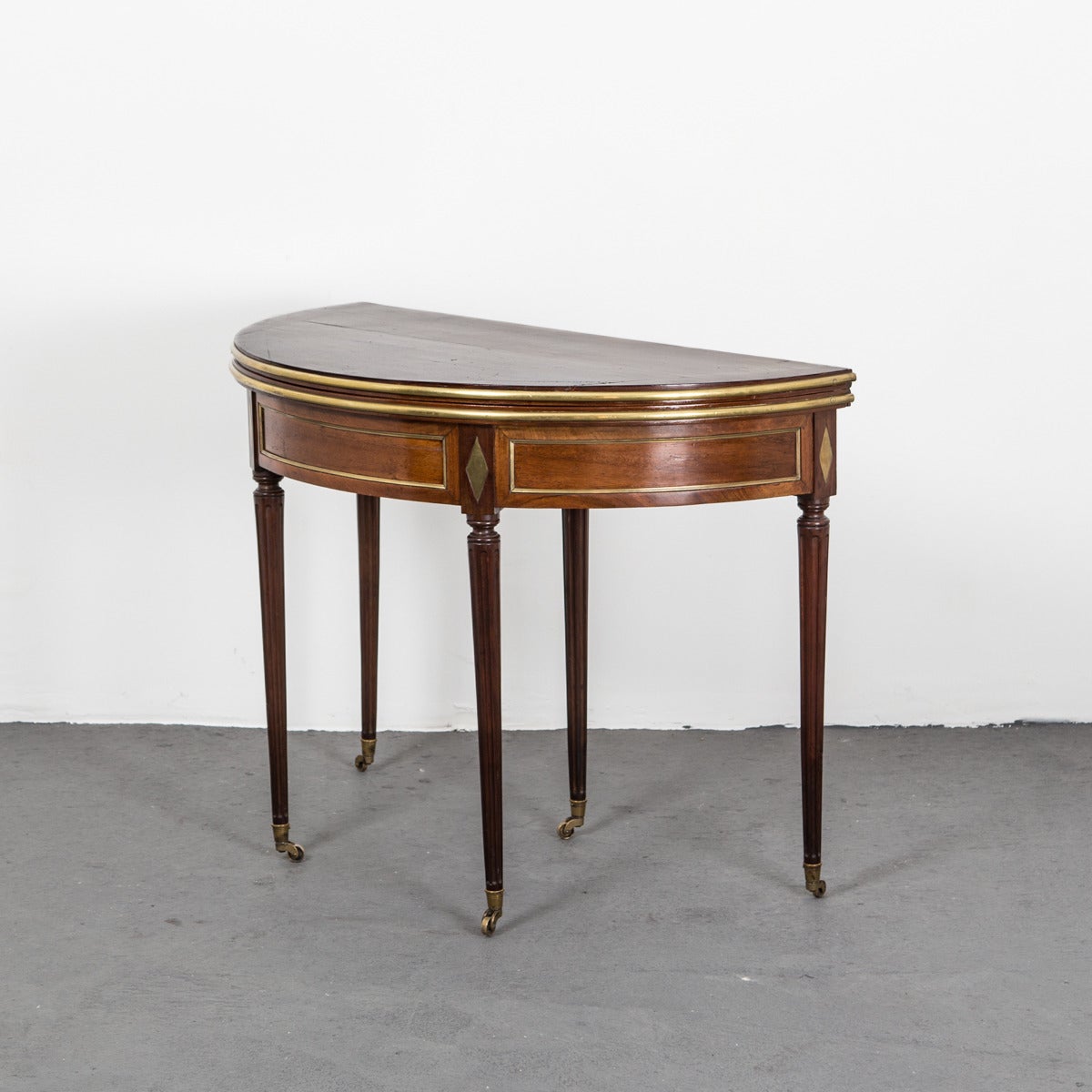 An extraordinary game table from the Directoire period made in France. Frame made of mahogany in a beautiful cognac brown shade. Apron divided into rectangular parts of brass and brass diamonds ending each leg. Five tapered legs with brass wheel