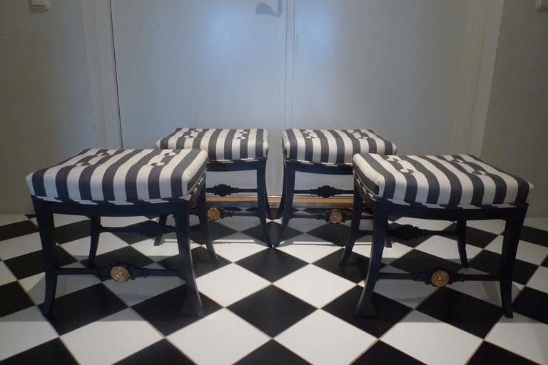 Set of four Karl Johan / Neoclassical stools in black painted wood made ca1810-1830. Gilded detail on cross beam. Upholstered in black and white striped cotton. Can be purchased as a pair.