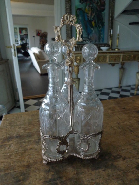 A carafe set of three crystal bottles with edged glass standing in a plated silver stand.