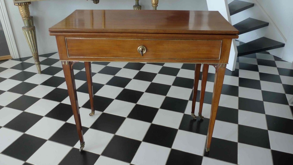 A lovely mahogany game table from the late Gustavian Period. Decorated with brass details and a wide drawer in frieze. The tapered legs ends with brass casters. Top folds out to twice the size.