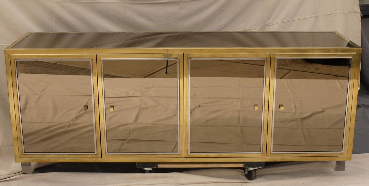 Large mirrored credenza designed by Michel Pigneres with brass and chrome doors and a laminate covered interior supported by Lucite legs. The construction on this cabinet is top notch.