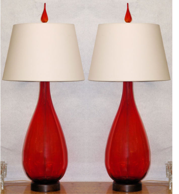 Pair of large ruby red lamps by the blenko company of west virginia with original finials and hardware.  Slight variation in these hand blown lamps.