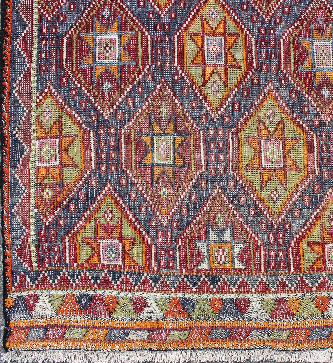 This embroidered flat-weave Jajeem bears a repeating diamond design with star and geometric motifs. Set on a multicolored blue and purple background, the accent colors are light green, red, yellow, orange, cream and brown.
Measures: 6'2 x 9'4.