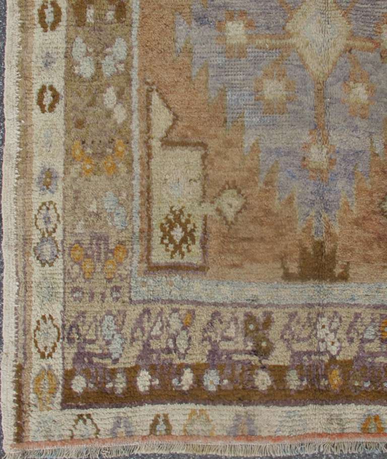This muted Oushak runner rests beautifully upon a field of elegant light gray and taupe. Three medallions of blue and brown take center stage and are well balanced by the broad border of light brown, green and taupe that gently surrounds the center